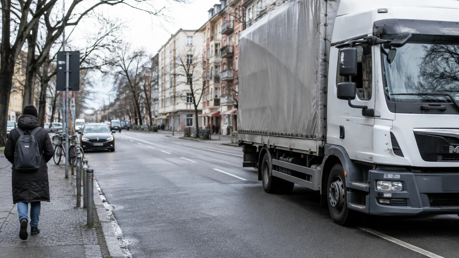 Ein weißer Lastwagen steht an einer städtischen Straße neben einem Gehweg mit Menschen.